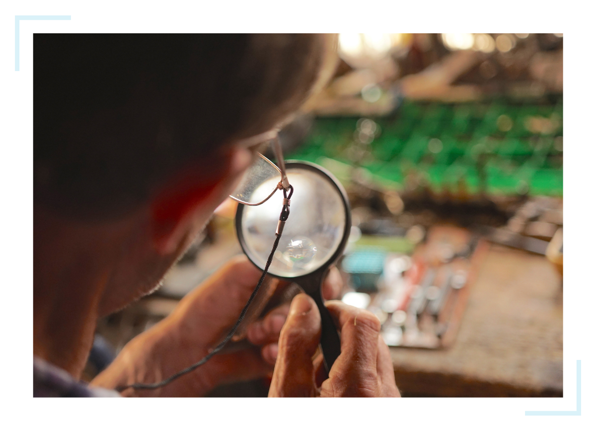 While providing custom electronic design services, a man wearing glasses examines an element through a magnifying glass.