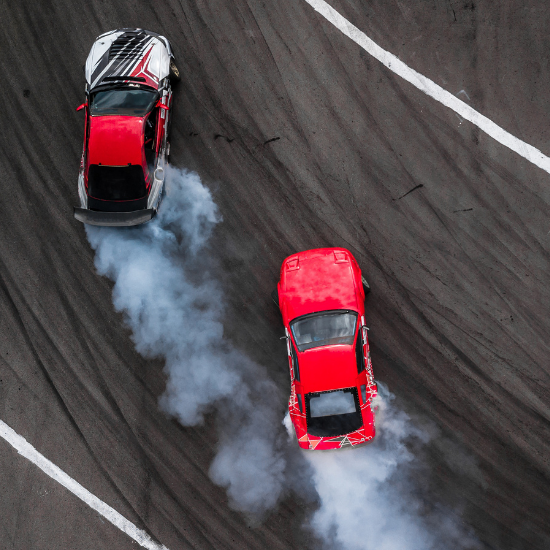 Two high performance cars race each other on a track. One is red and balck, the other is solid red.