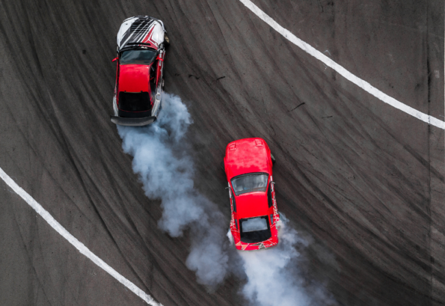Two high performance cars race each other on a track. One is red and balck, the other is solid red.