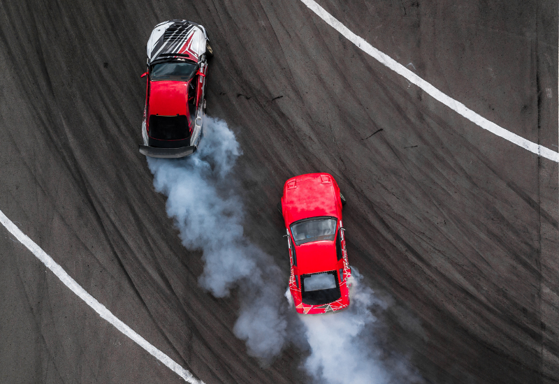 Two high performance cars race each other on a track. One is red and balck, the other is solid red.