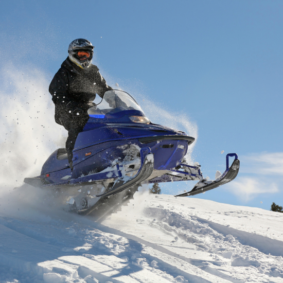 A person in a helmet and snowsuit jumps a snow mound while riding a snowmobile designed using electronics engineering.