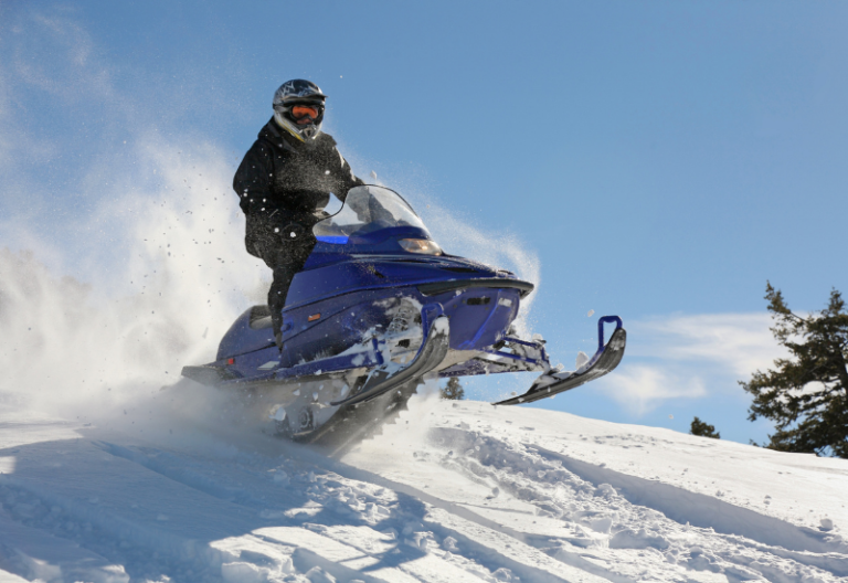 A person in a helmet and snowsuit jumps a snow mound while riding a snowmobile designed using electronics engineering.