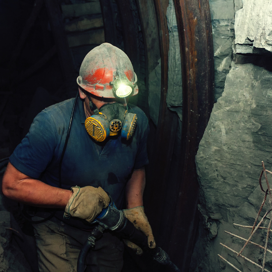 A man working in a mine wearing a hard hat with a light on it and a respirator mask. His work is made safer through tools created by advanced electrical engineering.
