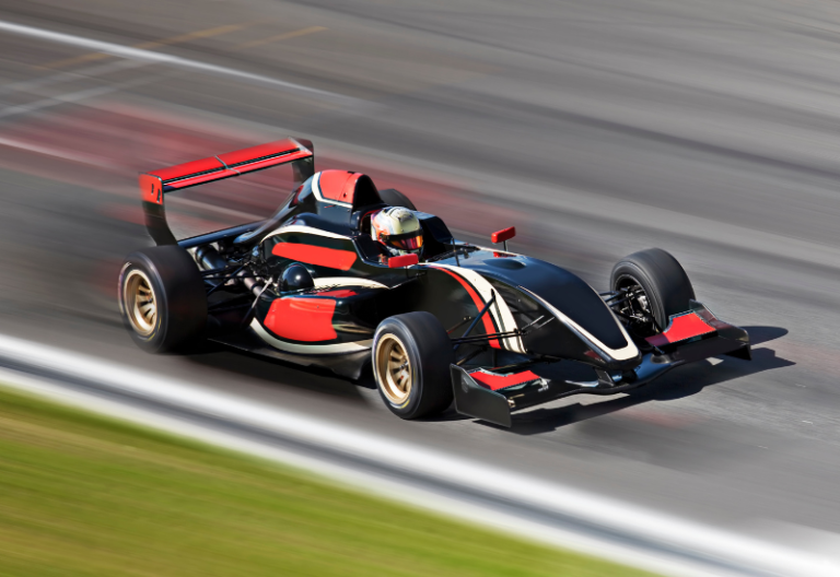 A red and black race car is in focus while the track around it is blurry, showing the care is moving very fast.