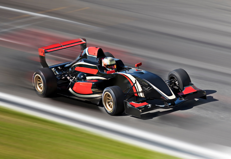A red and black race car is in focus while the track around it is blurry, showing the care is moving very fast.